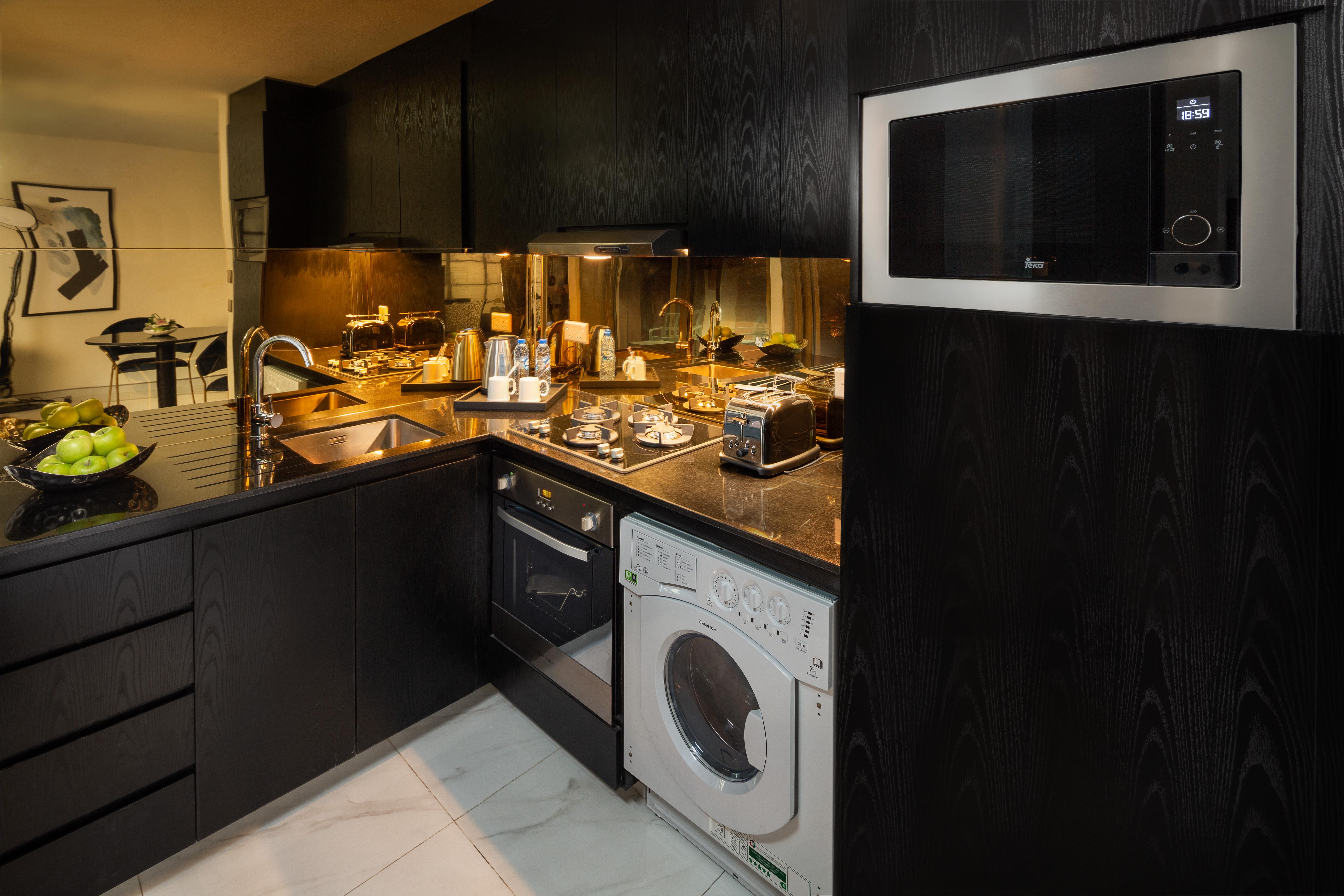 มิลเลนเนียม เอเตรีย บิสซิเนส เบย์ Aparthotel ดูไบ ภายนอก รูปภาพ The photo shows a modern kitchen with a sleek design featuring black cabinetry and countertops. There is a sink with a faucet, a stove with multiple burners, and an oven integrated into the cabinetry. A microwave is mounted above the counter for conv