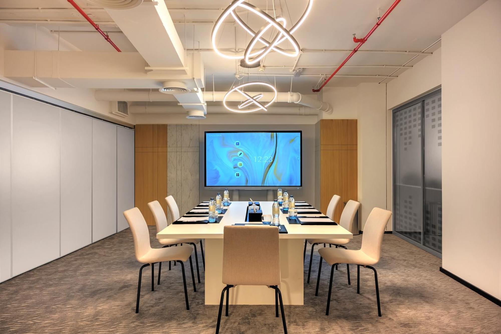 มิลเลนเนียม เอเตรีย บิสซิเนส เบย์ Aparthotel ดูไบ ภายนอก รูปภาพ The photo shows a modern conference room designed for meetings. It features a long white table surrounded by beige chairs. At the end of the table, there is a large screen displaying a blue abstract design. The room is well-lit with contemporary ligh