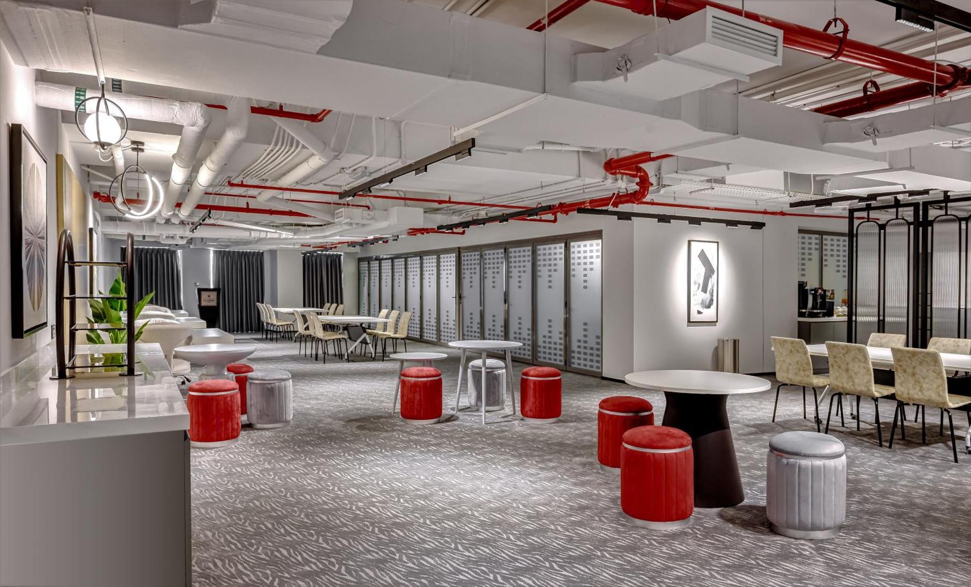 มิลเลนเนียม เอเตรีย บิสซิเนส เบย์ Aparthotel ดูไบ ภายนอก รูปภาพ The photo shows a modern interior space, likely an office or communal area. The flooring is covered with a textured carpet, and the ceiling features exposed pipes painted red. 

There are several seating options, including small round tables with sto