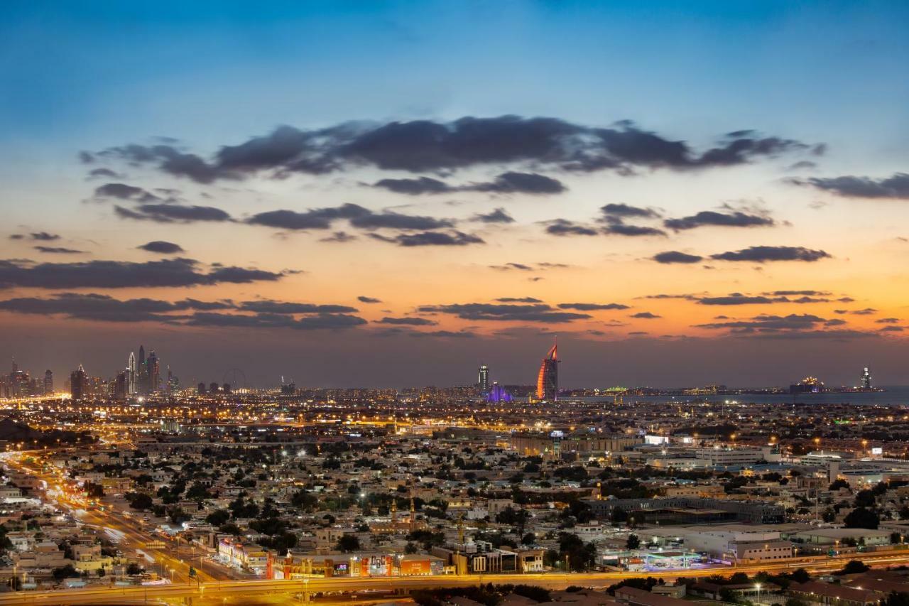 มิลเลนเนียม เอเตรีย บิสซิเนส เบย์ Aparthotel ดูไบ ภายนอก รูปภาพ The photo shows a stunning cityscape at dusk, with a panoramic view of a city skyline. The sky is transitioning from blue to orange, indicating sunset, with scattered clouds creating a colorful backdrop. In the foreground, you can see a sprawling urb