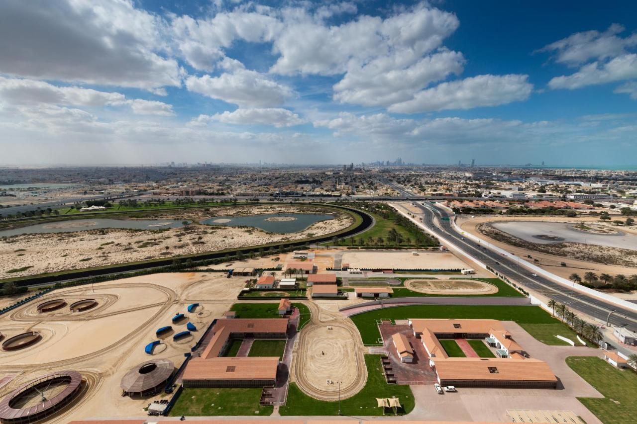 มิลเลนเนียม เอเตรีย บิสซิเนส เบย์ Aparthotel ดูไบ ภายนอก รูปภาพ The photo shows a panoramic view of a large landscape with expansive open areas, buildings, and a curved track. In the foreground, there are several stable structures and facilities associated with horse training or racing, surrounded by well-maintai
