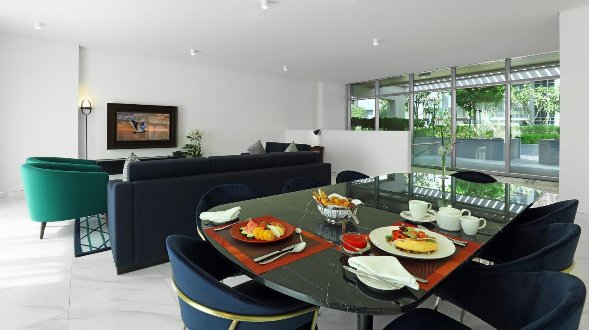 มิลเลนเนียม เอเตรีย บิสซิเนส เบย์ Aparthotel ดูไบ ภายนอก รูปภาพ The photo depicts a modern living space with a dining area and a seating area. In the foreground, there is a round dining table set with plates of food, including eggs, toast, and a small bowl of fruit, accompanied by cups and napkins. The table is c